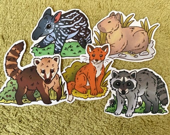 May include: Five colorful animal stickers with green foliage backgrounds. The stickers feature a red fox, a brown and white raccoon, a brown and white tapir, a brown and white coati, and a brown and white capybara.