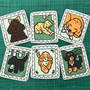 Op de afbeelding: Zes kleurrijke geïllustreerde kaarten met verschillende hondenrassen. Elke kaart heeft een witte rand en een witte achtergrond met een bruine, zwarte of oranje hond.