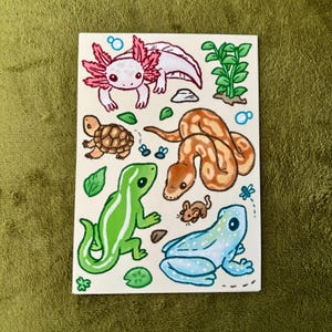 Puede incluir: Ilustración pintada a mano con varios reptiles y anfibios. La obra de arte incluye un ajolote rosa, una tortuga, un lagarto verde, una serpiente marrón, un ratón y una rana azul. El fondo es blanco con hojas verdes y burbujas.