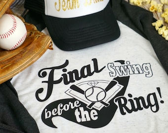 Może przedstawiać: Biała koszulka z czarnym nadrukiem w stylu baseballowym, na którym widnieje napis "Final Swing before the Ring!" W tle widoczny jest rękawica baseballowa i piłka baseballowa.