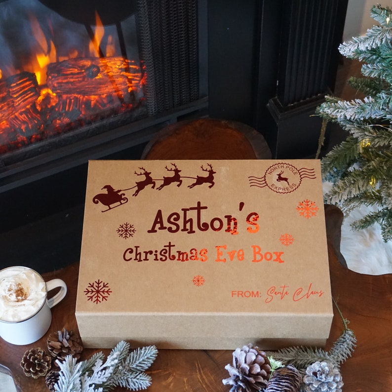 Holiday theme gift box for kids on a wood table with Christmas tree, pine cones and hot cocoa displayed.