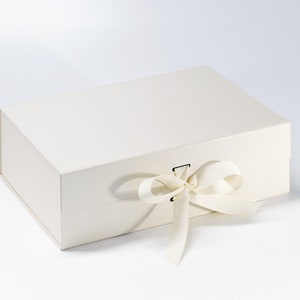 May include: A white gift box with a white satin ribbon tied in a bow. The box is closed and has a small metal clasp.