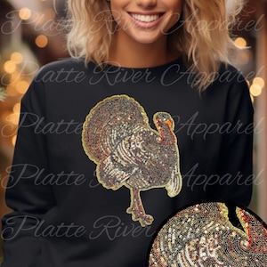 Könnte beinhalten: Schwarzes Sweatshirt mit einem detaillierten Truthahndesign aus echten Pailletten. Der Truthahn hat braune, goldene und rote Farbtöne. Der Text "Real Sequins!" ist gelb. Das Sweatshirt ist von Platte River Apparel.