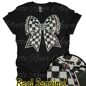 Può includere: T-shirt nero con un grande design a fiocco realizzato con paillettes nere, bianche e rosa. Il fiocco ha un motivo a scacchi ed è il punto focale della maglietta. Il testo "Real Sequins!" è visualizzato in basso.