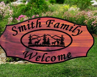 May include: A wooden welcome sign with a red-brown stain. The sign is oval shaped with a smaller oval in the center. The smaller oval features a silhouette of a mountain range with two deer and a person. The text "Smith Family Welcome" is carved into the sign.