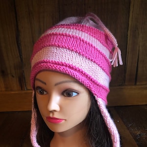 Könnte beinhalten: Rosa-weiß gestreifter Strickmütze mit langen Bändern. Die Mütze hat eine spitze Spitze und die Bänder sind unten zusammengebunden.