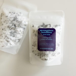 May include: Two clear pouches filled with bath soak. One pouch has a label that reads "strengthen intuition BATH SOAK" with a list of ingredients. The bath soak appears to contain white salts and dried herbs.