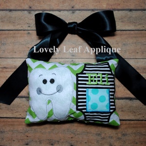 May include: A green and white pillow with a tooth and a black and white striped shirt with the name "Eli" embroidered on it. The pillow has a black ribbon tied around it.