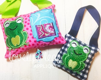Op de afbeelding: Twee kleine kussenachtige zakjes met geborduurde groene kikkers. Eén zakje is roze met witte stippen en een blauwe rand. Het andere zakje is zwart-wit geruit met een blauwe band. De tekst "lovely leaf applique" is zichtbaar onder de zakjes.