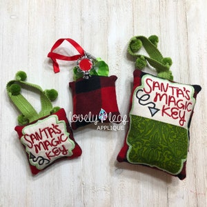 May include: Three red and green pillow ornaments with the text "Santa's Magic Key" embroidered on them. The ornaments are decorated with green pom-poms and a green ribbon.