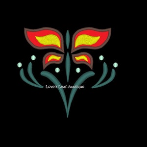 Puede incluir: Una aplicación de mariposa estilizada con alas rojas, amarillas y marrones, rodeada de hojas verde azuladas y puntos blancos. El texto "Lovely Leaf Applique" está debajo de la mariposa.