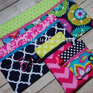May include: Five colorful zippered pouches with different patterns. The pouches are made of fabric and have a zipper closure. The pouches are stacked on top of each other. The top pouch is green with white polka dots. The second pouch is pink with a floral pattern. The third pouch is navy blue with a white geometric pattern. The fourth pouch is yellow with white polka dots. The fifth pouch is pink with a chevron pattern. The pouches are all decorated with a single initial.