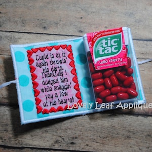 May include: A blue and white fabric pouch with a pink heart border and embroidered text that reads "Cupid is at it again throwin' his darts. Thankfully! dodged him while snaggin' you a few of his hearts!"  A small plastic container of Tic Tacs in wild cherry flavor is attached to the pouch.