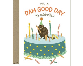 May include: A birthday card with a beaver wearing a party hat and holding a lit candle. The beaver is standing on a blue and green cake with yellow polka dots and surrounded by lit candles. The card reads "It's a DAM GOOD DAY to celebrate!"