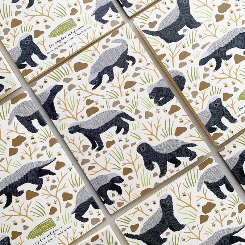 May include: A set of 10 notecards featuring a repeating pattern of honey badgers and bees on a white background. The notecards are printed with the text "Yeppe Paper Los Angeles, California www.yeppepaper.com made in USA".