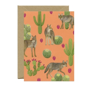 May include: A repeating pattern of coyotes and desert plants on a peach-colored background. The pattern includes cacti, prickly pear, and saguaro cacti. The coyotes are brown and gray with black noses and eyes.