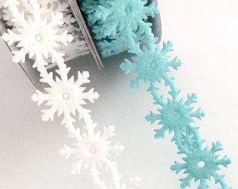 May include: Two spools of snowflake trim, one white and one light blue. The trim is made of fabric and has a delicate snowflake design.