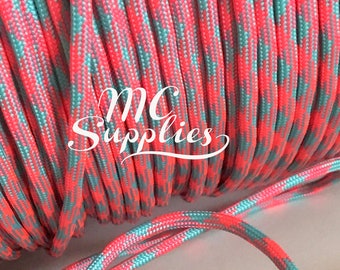 May include: A spool of pink and teal paracord with a checkered pattern. The paracord is coiled and a length of the cord is laying loose.