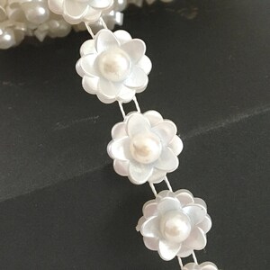 May include: White pearl flower trim with a pearl in the centre of each flower. The trim is on a spool and is ready to be used for crafting projects.