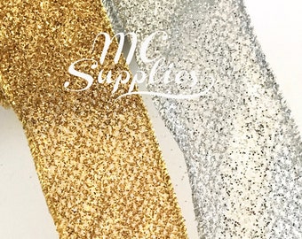 May include: Two rolls of glitter ribbon, one gold and one silver. The ribbon is textured and has a sparkly finish.