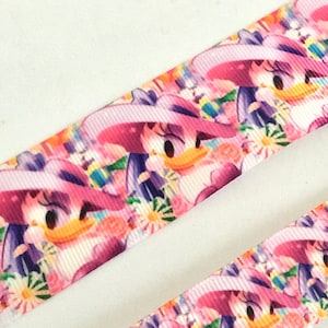 May include: Pink and white ribbon with a repeating pattern of a cartoon duck wearing a pink hat and flowers.