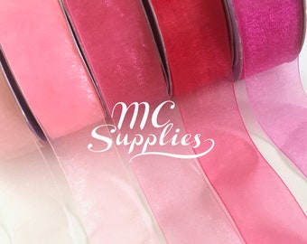 May include: Five rolls of sheer ribbon in various shades of pink, from white to a deep fuchsia. The ribbon is arranged in a fan shape, with the lightest shade at the bottom and the darkest shade at the top. The ribbon is perfect for adding a touch of elegance to any project.