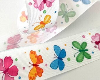 May include: White ribbon with a repeating pattern of colourful butterflies and small dots. The butterflies are in various colours, including blue, green, pink, orange, and yellow.