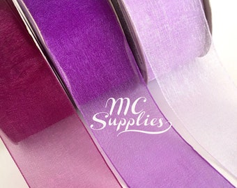 May include: Three rolls of sheer ribbon in shades of purple, pink, and white. The ribbon is ombre, with the color gradually fading from dark to light.