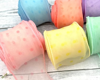 May include: Six spools of sheer ribbon with polka dots in various pastel colors, including pink, yellow, light blue, green, and purple. The ribbon is rolled up and displayed on a white wooden surface.