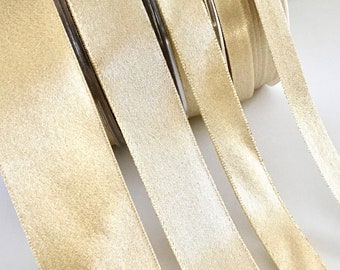 May include: Close-up of several spools of gold satin ribbon. The ribbon is unwound, showing its smooth texture and sheen. Suitable for crafts, gift wrapping, or decorative use. Each spool is a different length.