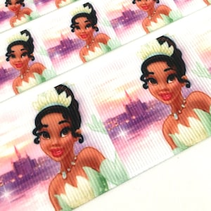 May include: White satin ribbon with a repeating pattern of a cartoon princess with brown skin, a green dress, and a crown. The princess is looking to the right and the background is a purple and pink cityscape.