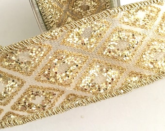 May include: Gold glitter ribbon with a white geometric pattern. The ribbon has a wired edge and is on a spool.