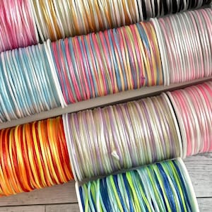 May include: A collection of spools of colorful embroidery floss, including pink, blue, yellow, orange, green, and white. The spools are arranged in a row on a wooden surface.
