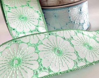 May include: Four rolls of white ribbon with a green floral pattern. The ribbon is made of a sheer fabric with a delicate lace design.