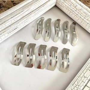 May include: A set of ten silver hair clips. The clips are all the same size and shape, and they have a wavy design. They are arranged in two rows on a white background.