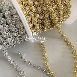 May include: Two spools of rhinestone trim, one gold and one silver. The trim features a repeating pattern of small, clear rhinestones set in a flower shape.