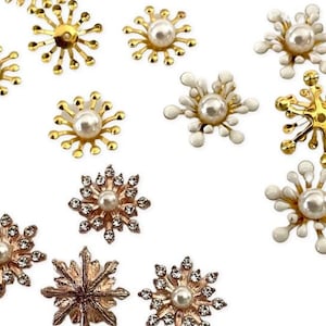 May include: Assortment of gold, white, and rose gold snowflake embellishments with pearl centers. The snowflakes are various sizes and styles.