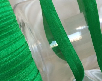 May include: A roll of bright green elastic ribbon with a folded edge. The ribbon is next to a clear container and a length of the ribbon is unrolled. The text "MC Supplies" is in white script.