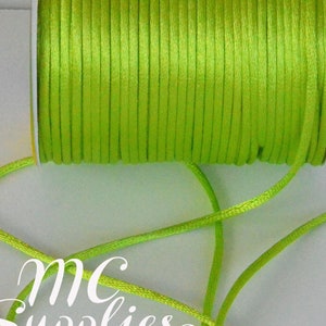 May include: A spool of bright green satin cord, with a length of the cord laid out on a white surface. The cord is smooth and shiny.
