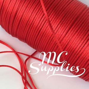 May include: A spool of red satin cord, with a length of the cord lying on a white surface. The spool is labeled "MC Supplies".