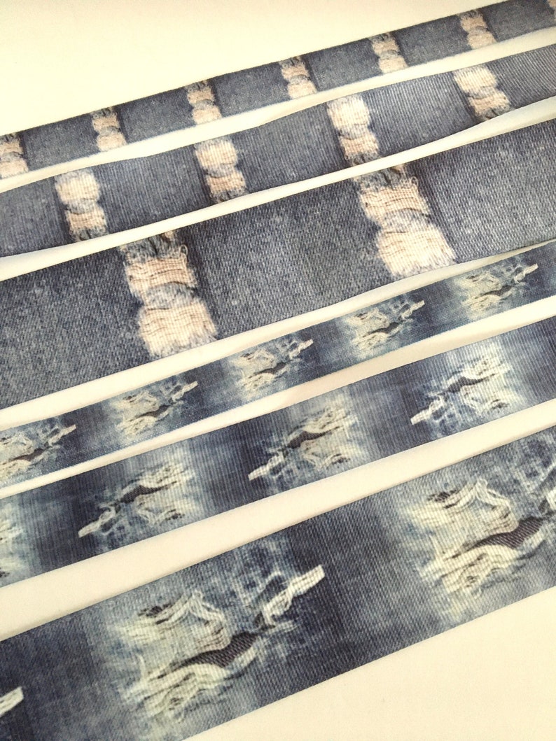 May include: Five different widths of blue and white denim-patterned ribbon. The ribbon has a distressed look with white rips and tears.