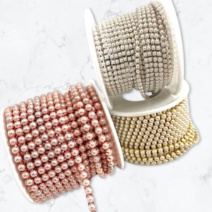 May include: Three spools of pearl trim, one in rose gold, one in gold, and one in silver. Each spool is wound with a continuous strand of small, round pearls.