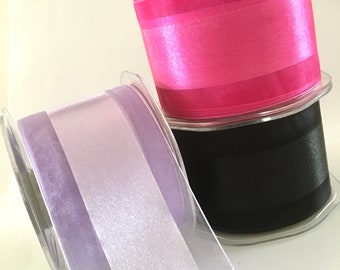 May include: Three spools of ribbon with satin and sheer fabric. The ribbon is in shades of pink, lavender, and black.
