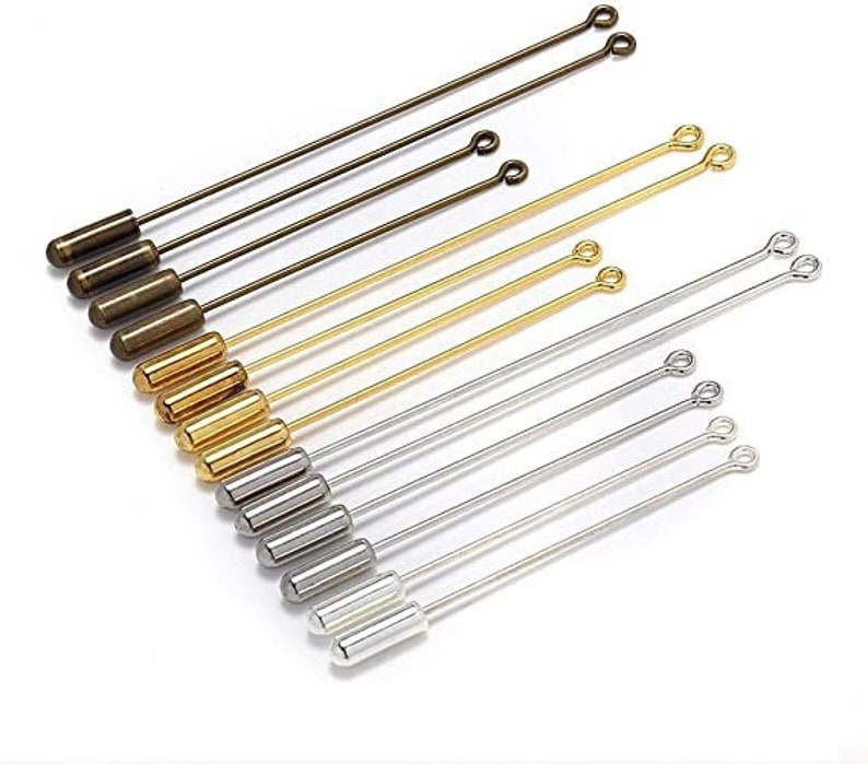 May include: A set of 10 gold, silver, and bronze safety pin style hat pins with a loop at the top and a rounded end. The pins are arranged in a row, with the gold pins at the top, the silver pins in the middle, and the bronze pins at the bottom.