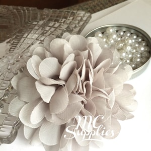 May include: A large, gray fabric flower with a ruffled texture. The flower is made of soft, delicate material and has a layered design.