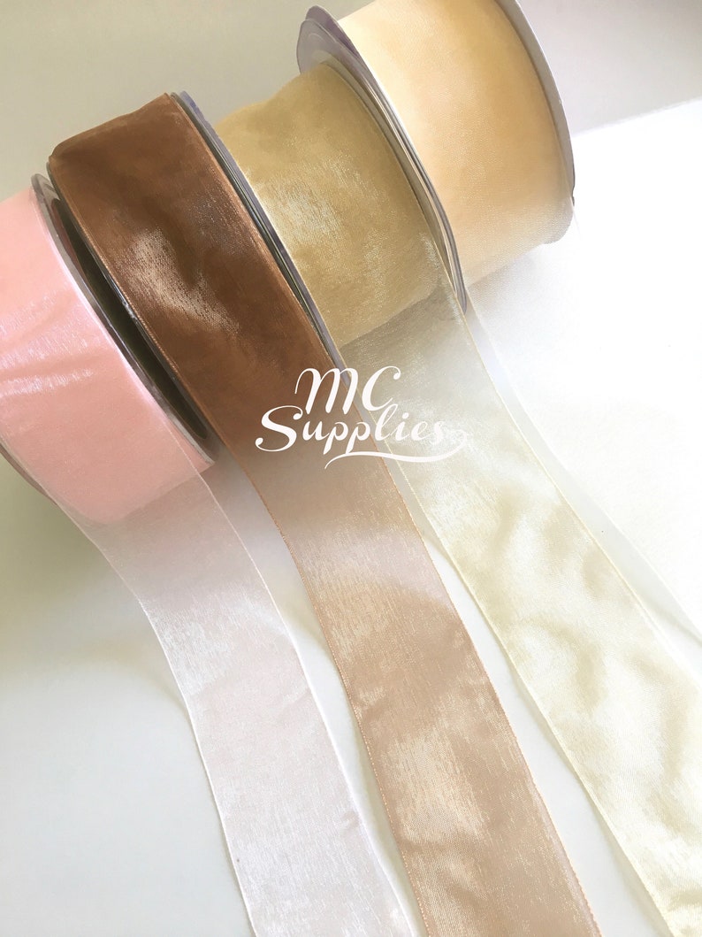 May include: Four rolls of sheer ribbon in pink, ivory, beige, and brown. The ribbon is rolled and tied with a white ribbon. The text "MC Supplies" is visible on the ribbon.
