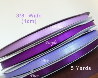 May include: Five spools of satin ribbon in shades of purple, orchid, iris, and plum. Each spool is 3/8 inch wide (1 cm) and 5 yards long. The spools are labeled with the color names and the text "MC Supplies".