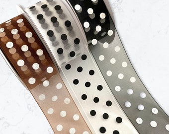 May include: Three rolls of sheer ribbon with white polka dots on a brown, gray, and black background.