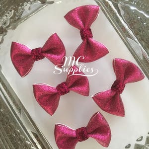 May include: Five pink glitter hair bows with a white center. The bows are arranged in a circle on a white surface. The text "MC Supplies" is visible in the center of the image.