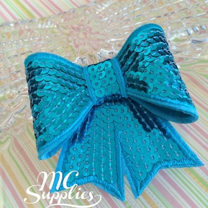 May include: A turquoise blue sequin bow with a satin finish. The bow is sewn with a decorative stitch around the edges.